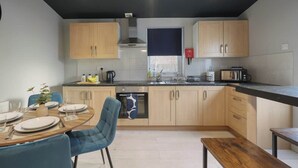 Eine moderne Küche mit Holzausstattung, einer schwarzen Arbeitsplatte und einem Essbereich mit blauem Stuhl und Holztisch.