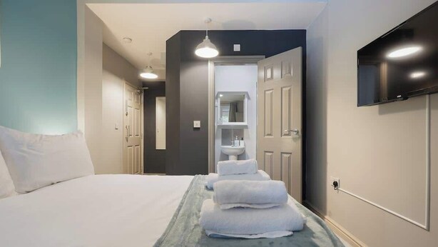 Ein Hotelzimmer mit einem Bett, einem Stapel blauer Handtücher, einem an der Wand montierten Fernseher und einer Tür zu einem Badezimmer.