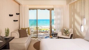 Habitació d'hotel moderna amb un llit gran, zona de seients amb vista a la platja i un balcó amb taula i cadires.