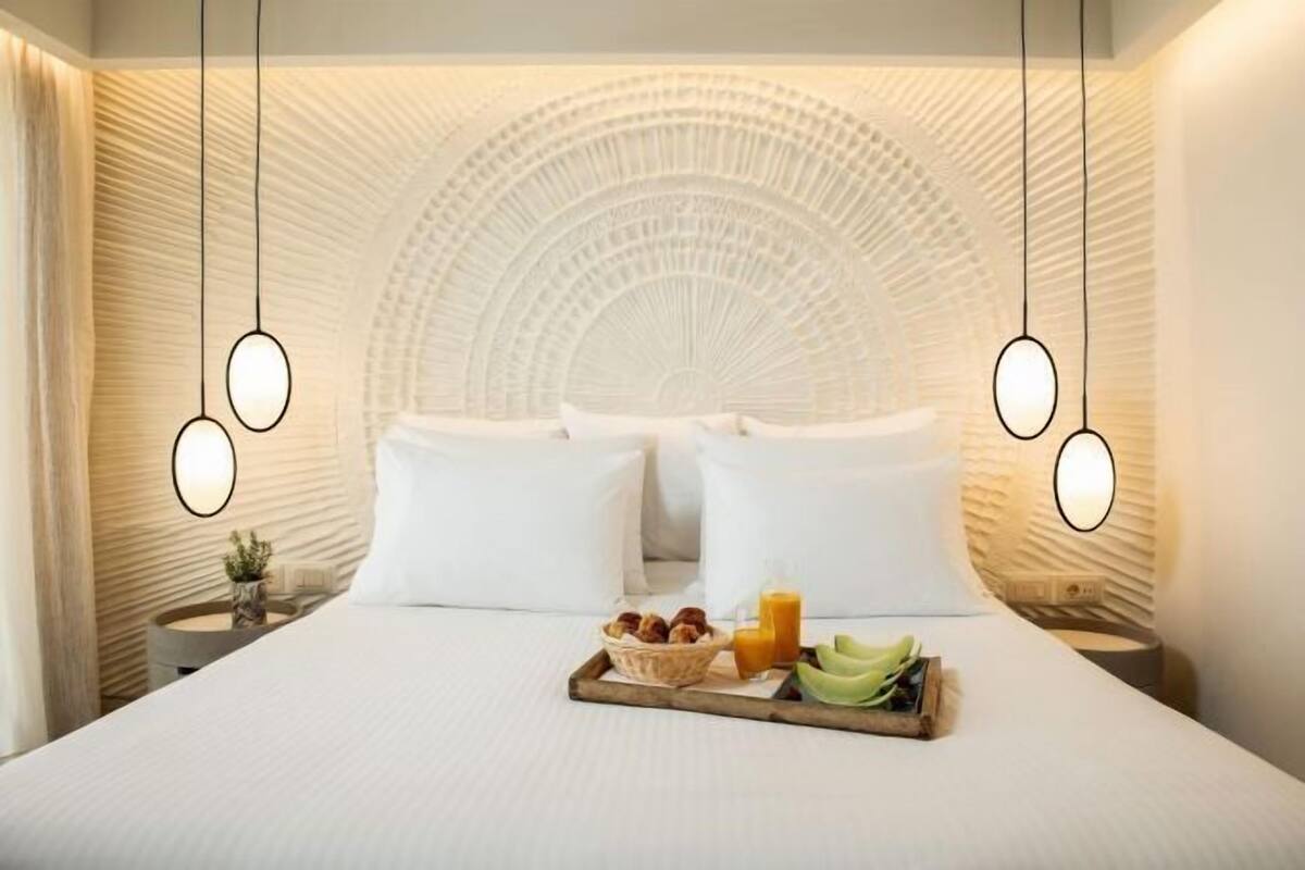 A hotel room with a bed, two bedside tables, a tray with breakfast items, and a unique ceiling design.