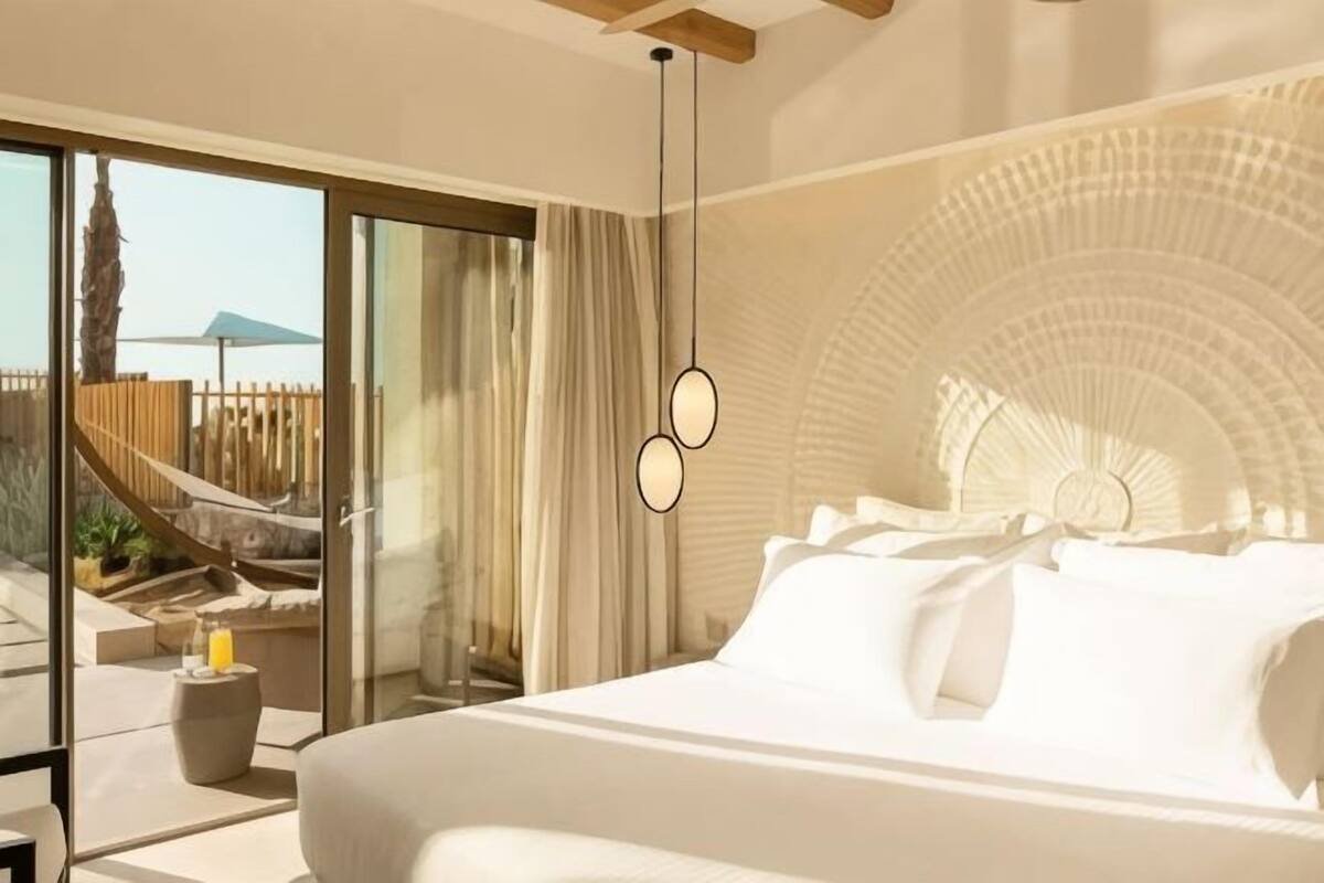 A modern bedroom with a large bed, a glass door leading to a balcony, and a unique ceiling design.