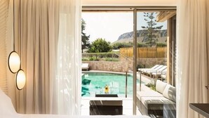 Habitació d'hotel amb un llit gran, vista a una piscina i un balcó amb seients exteriors.