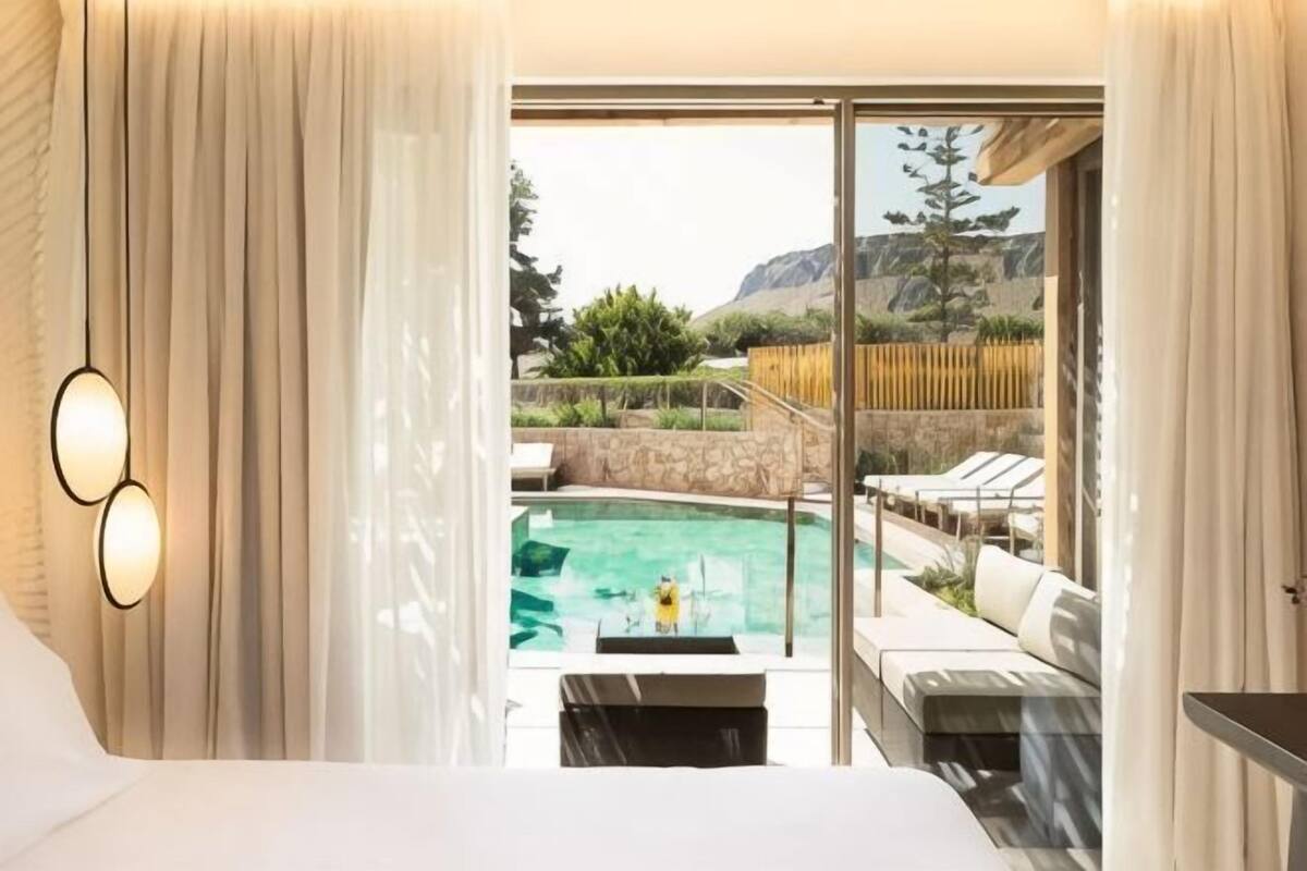 A hotel room with a large bed, a view of a swimming pool, and a balcony with outdoor seating.