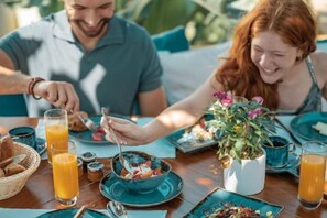 Una mesa de comedor con alimentos para el desayuno, una planta en maceta y un vaso de jugo de naranja.