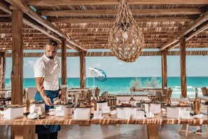 Ein Essbereich mit Holztisch, gedeckt für Gäste, mit Blick auf einen Strand.