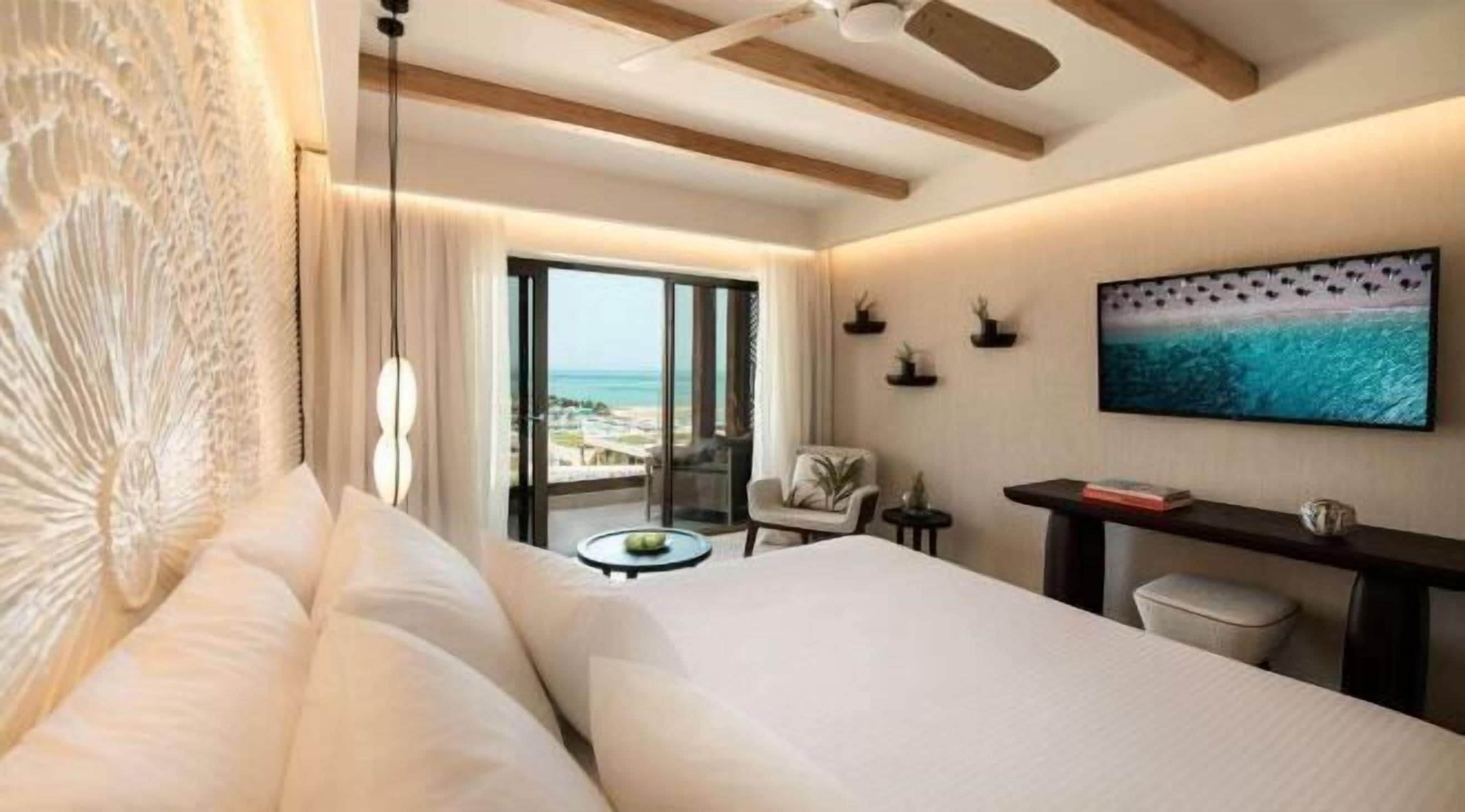 Habitación de hotel con cama, escritorio, silla, televisión y vista a la playa.