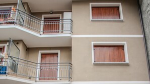 Un edificio residencial de varios pisos con balcones, un coche blanco estacionado y pavimento de piedra.