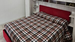 Un dormitorio con una cama, cabecera roja, armario blanco y una lámpara de techo circular.