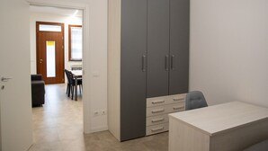 Una habitación con un armario grande de color gris, un escritorio pequeño y una zona de comedor con sillas y una mesa.