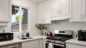 Eine moderne Küche mit weißen Schränken, Edelstahlgeräten und einem Fenster mit Jalousien.