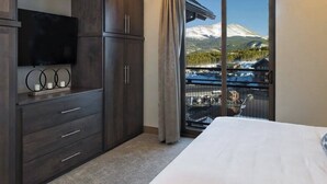 Un dormitorio con una cama grande, un armario de madera oscura, un televisor de pantalla plana y vistas a una montaña nevada desde un balcón.