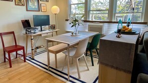 Una cocina moderna con una mesa de comedor, sillas, una laptop en un escritorio y un ventanal con vistas a árboles.