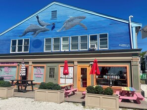 A blue building with a mural of dolphins, a Grilled Cheese Gallery, outdoor seating, and a Bubble Milk Tea sign.