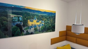 A room with a large landscape painting of a castle, a modern light fixture, and a sofa with a yellow pillow. - Smart, central apartment - garden - barbecue (Bückeburg)
