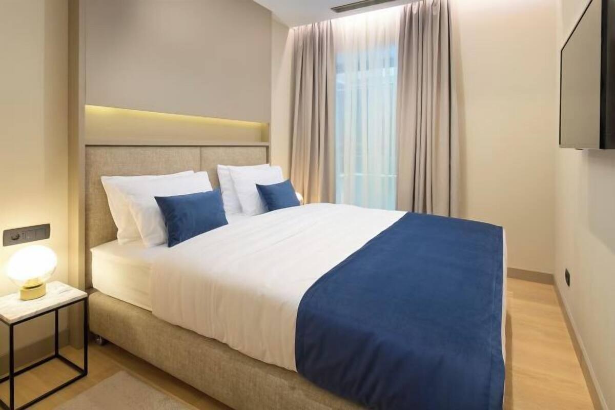 Una habitación de hotel ordenada con una cama, una mesita de noche y un televisor montado en la pared.
