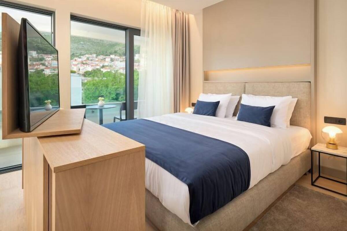 Habitación de hotel con cama, televisión, escritorio y vistas a un paisaje urbano.