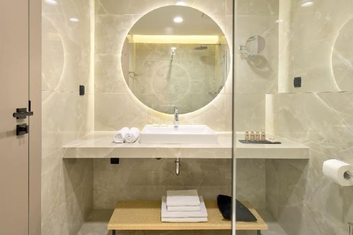 Une salle de bain moderne avec un miroir rond, un lavabo et un porte-serviettes.