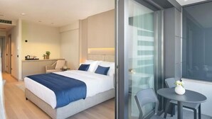 Ein modernes Hotelzimmer mit Bett, kleinem Tisch mit Stühlen, einer Glastrennwand und Blick ins Freie.