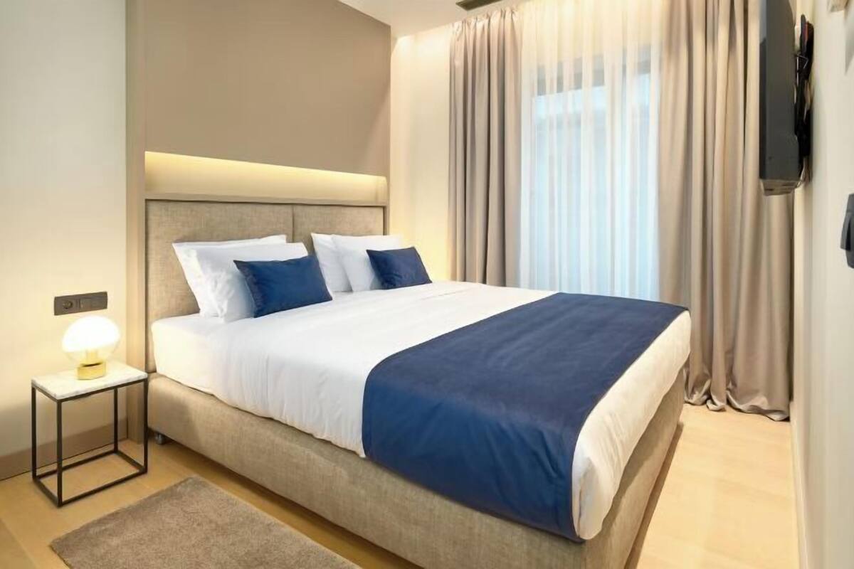 Habitación de hotel con cama, lámpara de noche, televisión de pantalla plana y ventana con cortinas.