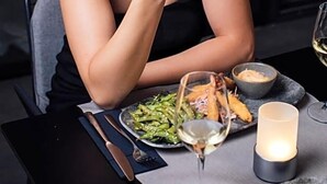 Eine Person sitzt an einem Tisch mit einem Teller Essen, einem Weinglas und einer Kerze.