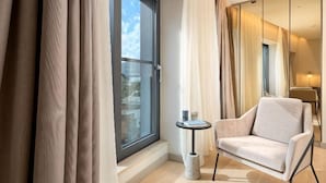 Ein modernes Hotelzimmer mit großem Fenster, einer Couch, einem kleinen Tisch und einer Lampe.