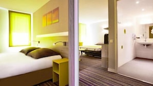 Habitació d'hotel moderna amb llit, taula de nit i bany amb rentapans i mirall.