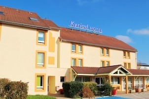 A hotel with a yellow facade, a sign reading "Kyriad Hotel," and a covered outdoor area with a pool.