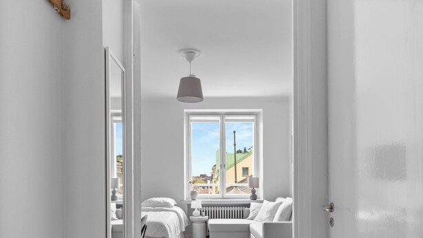 A hallway leading to a bedroom with a bed, a radiator, and a window.