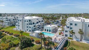 A multi-story hotel with a central courtyard featuring a swimming pool, surrounded by lush landscaping and palm trees. - Ocean View, 2 Primary Suites, Heated Pool, Beach (Cape Canaveral)