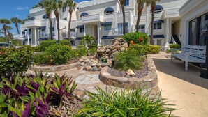 A hotel with multiple balconies, palm trees, and a landscaped garden with rocks and plants. - Ocean View, 2 Primary Suites, Heated Pool, Beach (Cape Canaveral)