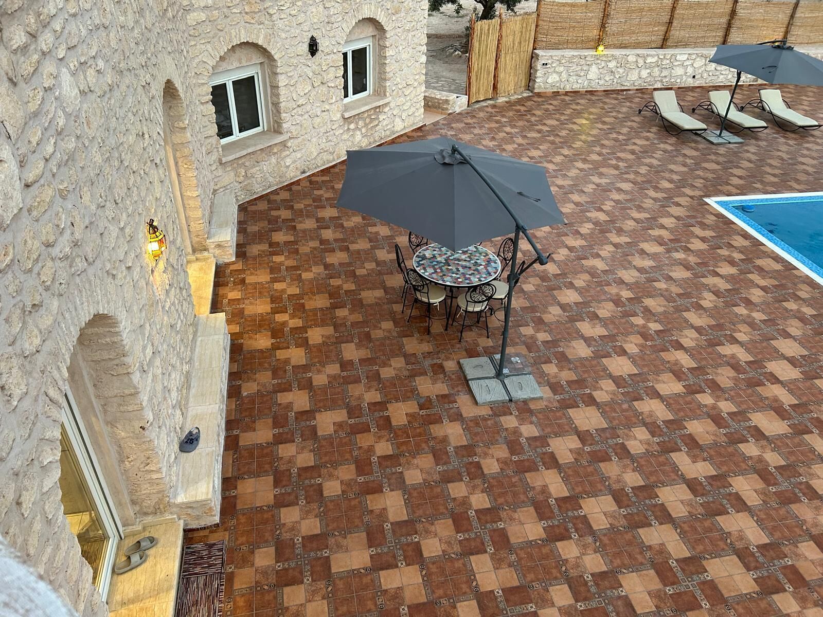 Une cour avec un sol carrelé, une table ronde entourée de chaises et une piscine.