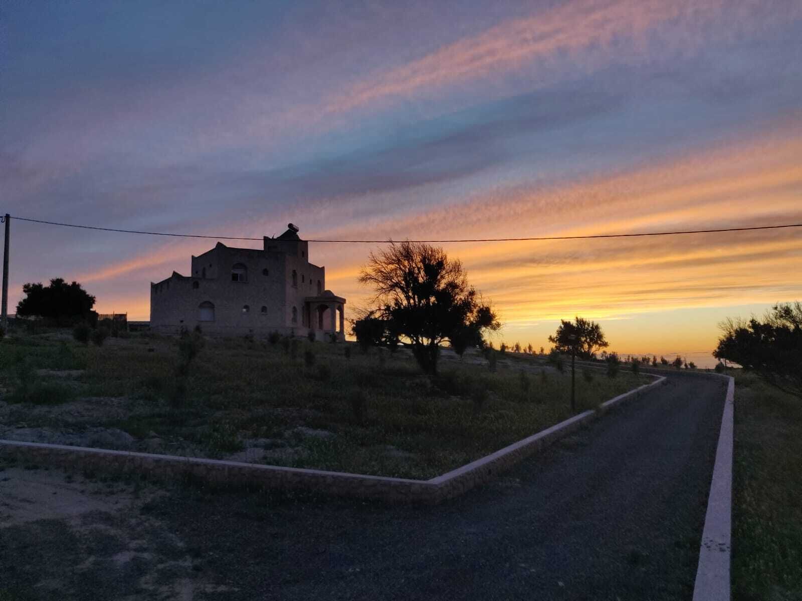 A rural road with a building on the left and a tree on the right.