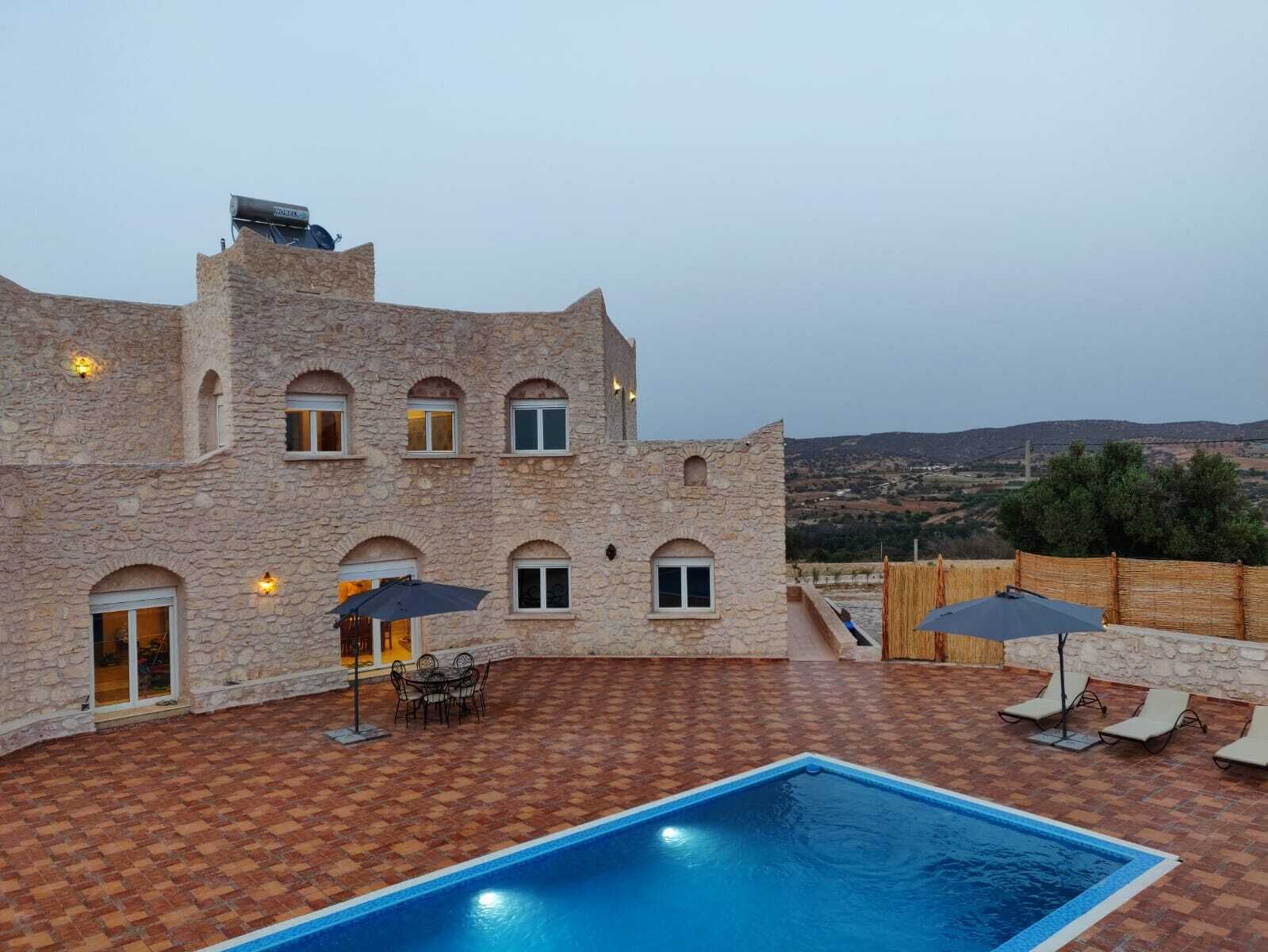 Un edificio de piedra con piscina, mobiliario exterior y vistas al campo.