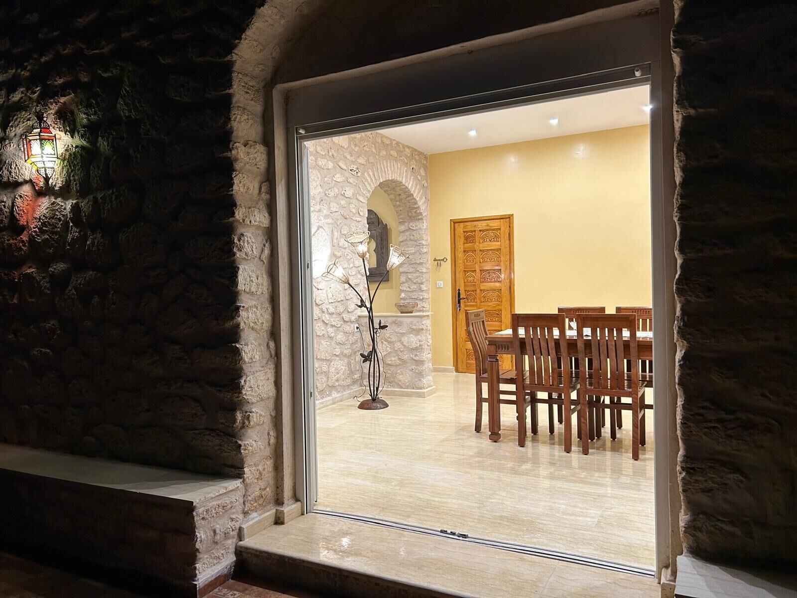 A stone-walled room with a dining area featuring wooden chairs and a table.