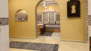 A hallway with a yellow wall, an archway leading to a room with a bed, a table, and a patterned rug. - Essaouira countryside, villa, swimming pool, 2 hectares, olive trees, mountain view, .... (essaouira)
