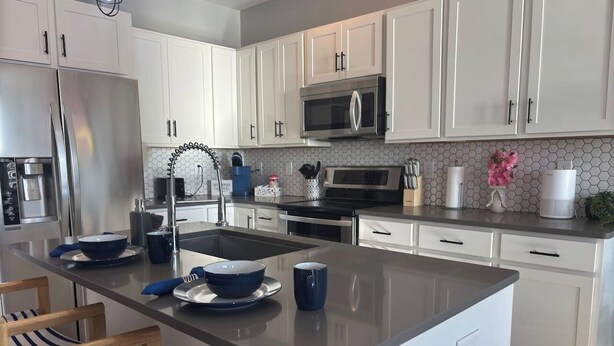Una cocina moderna con armarios blancos, electrodomésticos de acero inoxidable y una isla central con asientos.