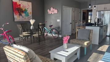 A modern living room with a dining area, kitchen, and a large abstract painting on the wall.