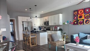 Una cocina moderna con armarios blancos, una isla central y una zona de comedor con mesa y sillas de vidrio.