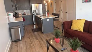 A modern kitchen with grey cabinets, a stainless steel refrigerator, and a central island. - Gated 2BR in Greenville w/Vibes (Greenville)