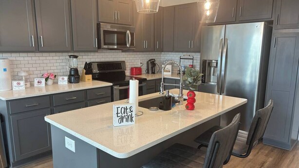 A modern kitchen with grey cabinets, stainless steel appliances, and a central island with seating. - Gated 2BR in Greenville w/Vibes (Greenville)