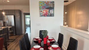 A modern dining area with a black table set for six, surrounded by black chairs. A colorful abstract painting hangs on the wall above the table. - Gated 2BR in Greenville w/Vibes (Greenville)