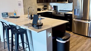 A modern kitchen with dark wooden cabinets, stainless steel appliances, a marble countertop, and black bar stools. - King Sky Suite | 1 Mile to Piedmont Park | Parking (Atlanta)