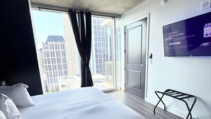 A hotel room with a large bed, a TV mounted on the wall, and a view of tall buildings through the window. - King Sky Suite | 1 Mile to Piedmont Park | Parking (Atlanta)