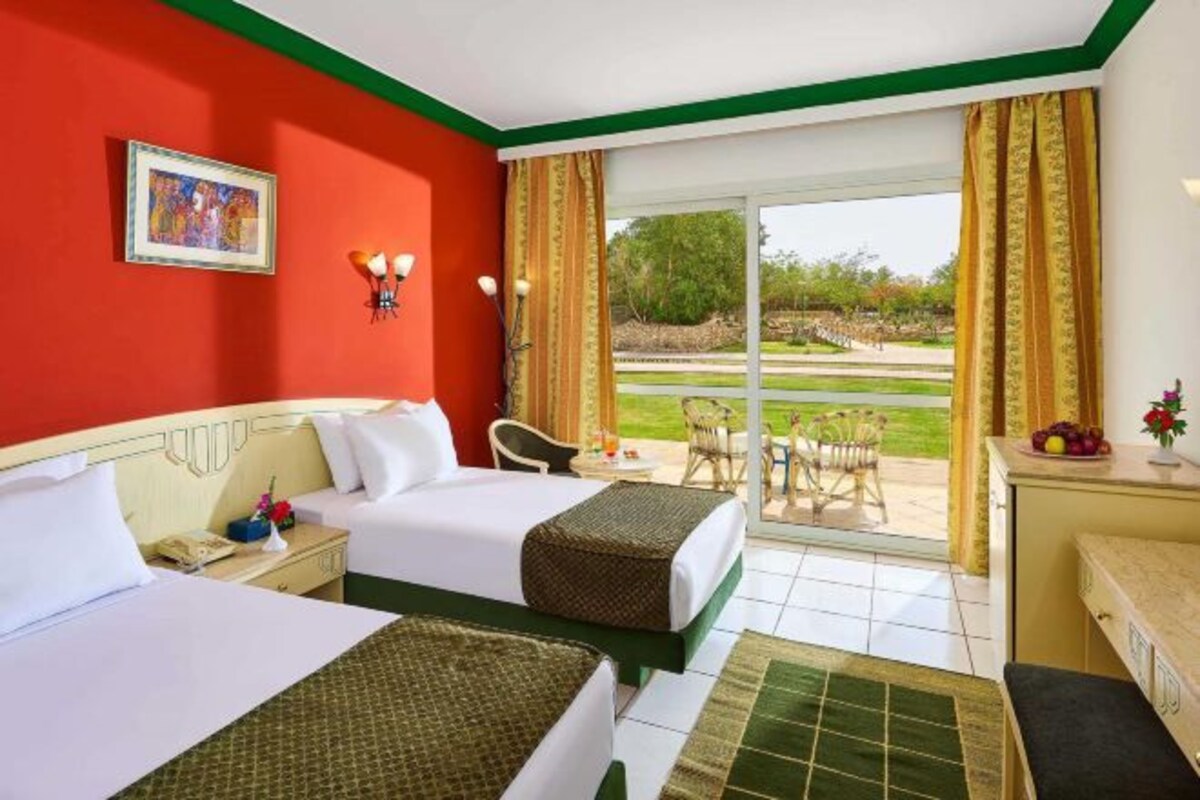A hotel room with two beds, a desk, a chair, and a view of the outdoors.