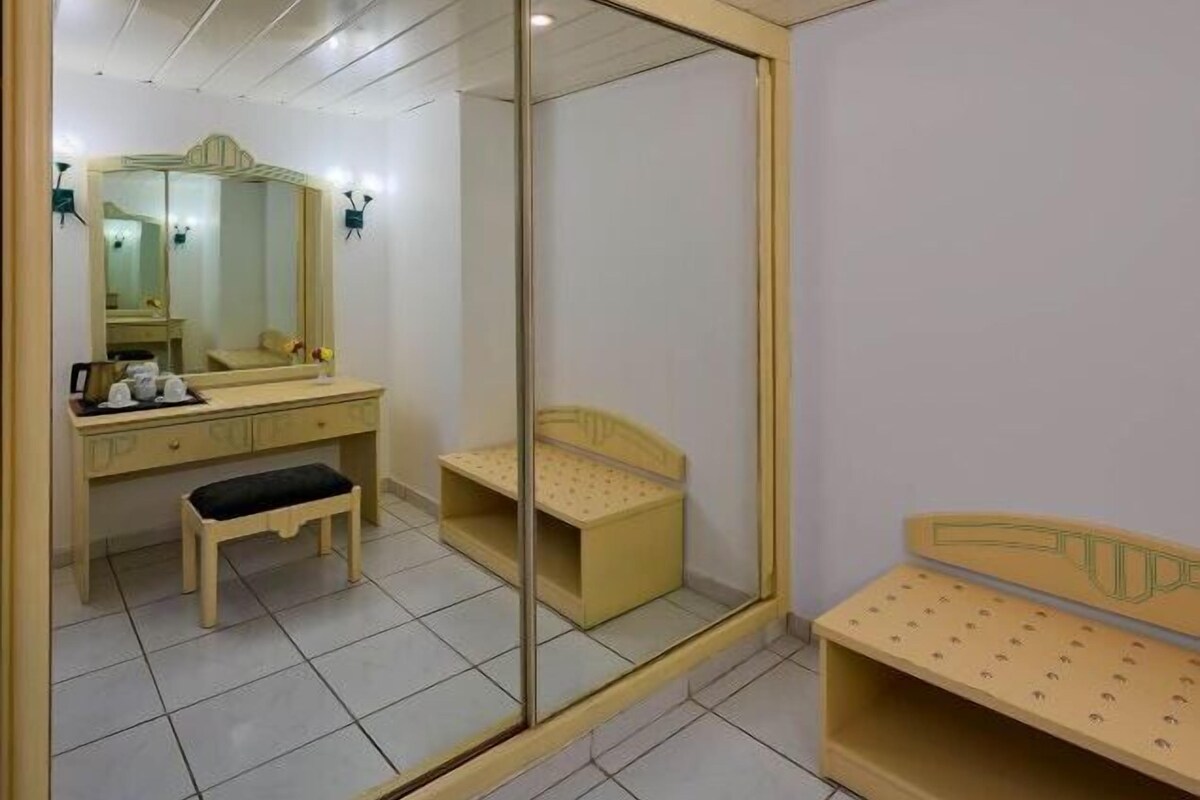 Une pièce avec un miroir, un banc en bois, une petite table et un meuble.