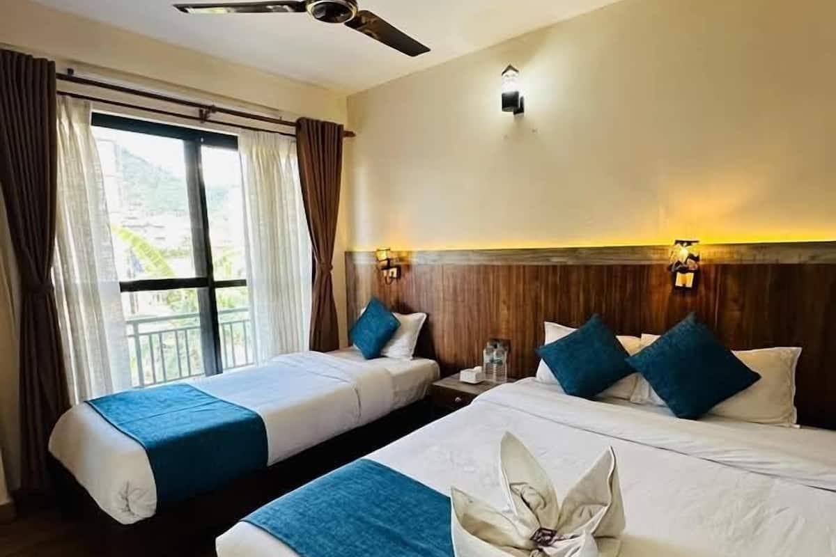 Ein Hotelzimmer mit zwei Betten, einem Deckenventilator, einem großen Fenster mit Vorhängen und Blick auf Grünfläche.