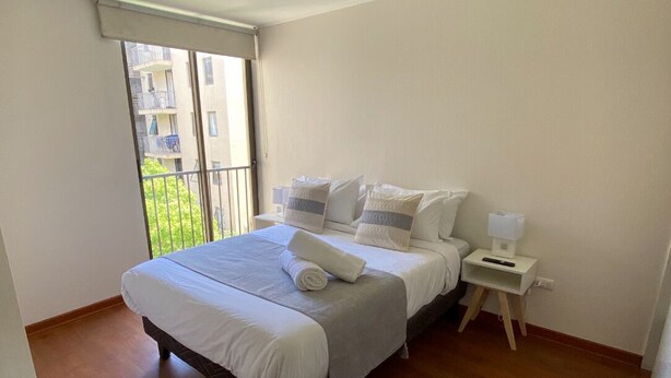 A bedroom with a bed, a nightstand, a window, and a view of buildings outside. - The most comfortable apartment in San Fernando (San Fernando)