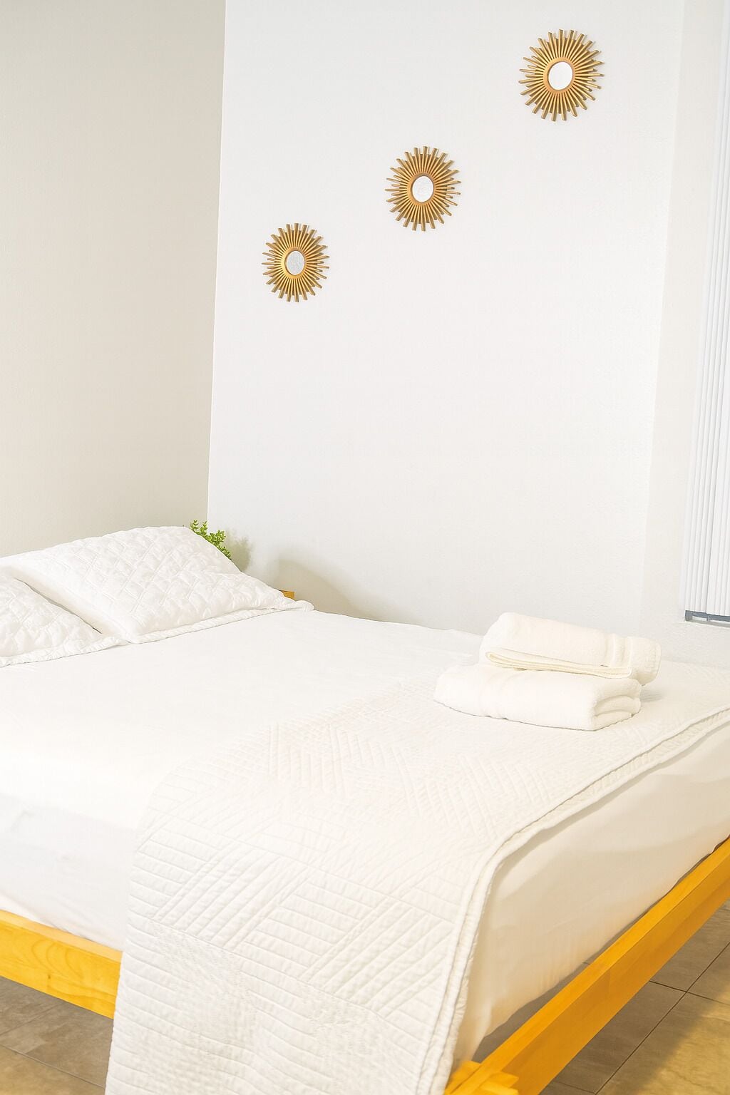 Un lit avec une couette blanche matelassée et des oreillers, une serviette pliée, et trois décorations murales en forme de soleil.
