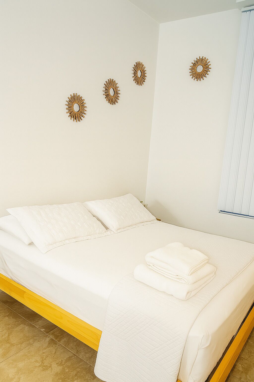 A bed with white bedding, a folded towel, and three wall-mounted sunburst mirrors.
