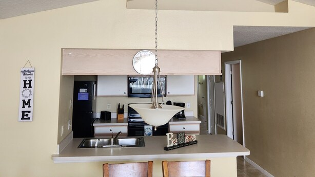 A modern kitchen with a built-in island, a hanging light fixture, and a welcome sign. - 3-bedroom condo in welcoming Kissimmee with WiFi, AC and Gated community. (Kissimmee)